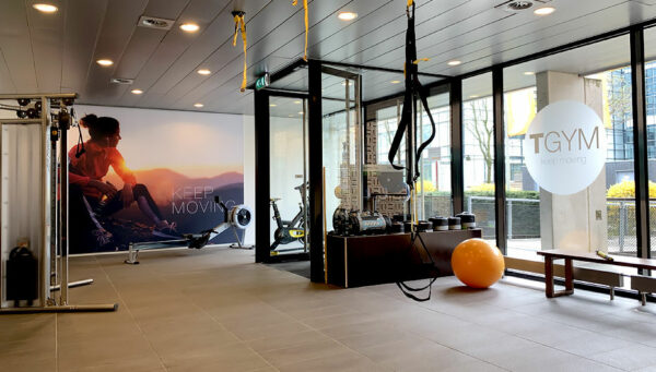 Moderne fitnessruimte bij TGYM aan de Laan van Vredenoord 33 met fitnessapparatuur, een oranje oefenbal en grote ramen.