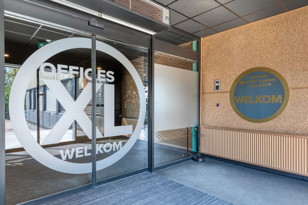 Ingang van het kantoorgebouw Offices XL aan de Laapvelderweg 15 met automatische schuifdeur en welkomstbord bij de intercom.