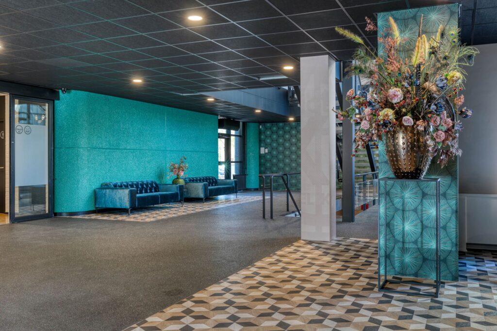 Moderne en kleurrijke lobby aan de Laapvelderweg 15 met blauwe zitbanken, grafische vloertegels en een grote decoratieve bloemenvaas.