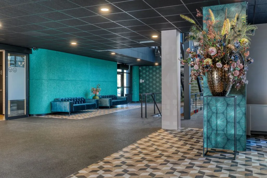 Moderne en kleurrijke lobby aan de Laapvelderweg 15 met blauwe zitbanken, grafische vloertegels en een grote decoratieve bloemenvaas.