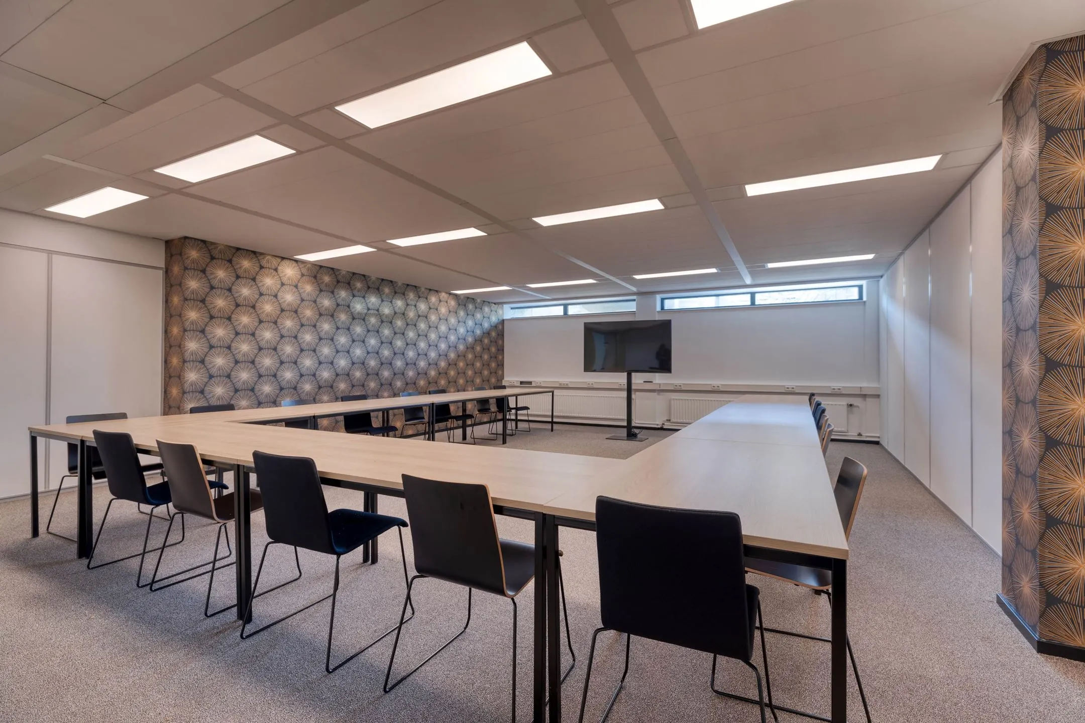 Vergaderruimte aan de Laapvelderweg 15 met U-vormige opstelling, moderne stoelen, een scherm en decoratief behang.