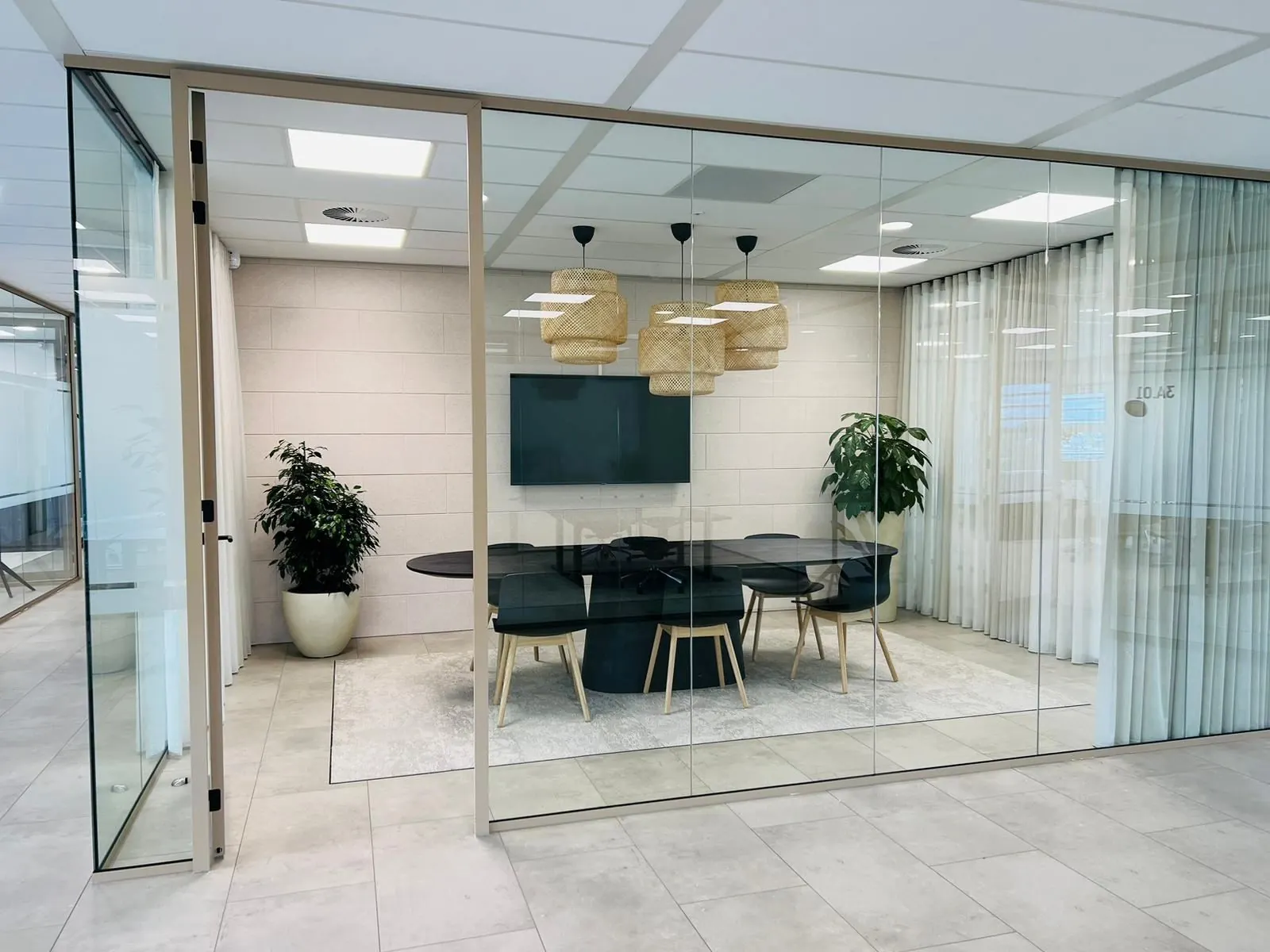 Vergaderruimte aan de Laarderhoogtweg 7 met glazen wanden, een ronde tafel, zes stoelen, planten en een flatscreen aan de muur.