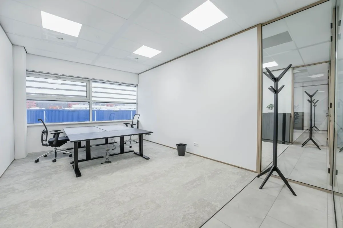 Moderne, lichte kantoorruimte aan de Laarderhoogtweg 7 met twee bureaustoelen, een groot bureau, een kapstok en grote ramen met uitzicht naar buiten.
