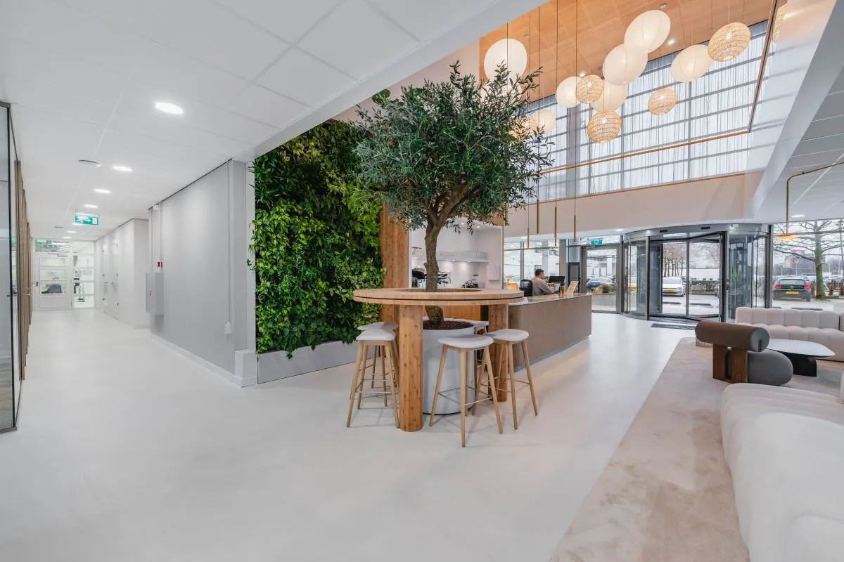 Moderne kantoorentree aan de Laarderhoogtweg 7 met een groene wand, een boomtafel en een ontvangstruimte met veel daglicht.