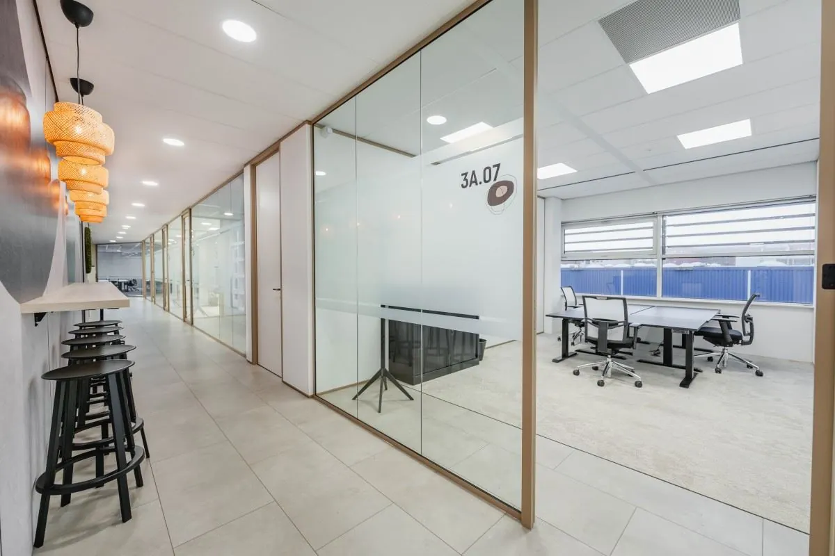 Moderne kantoorruimte aan de Laarderhoogtweg 7 met glazen vergaderruimte 3A.07 en een stijlvolle gang met barkrukken en hanglampen.