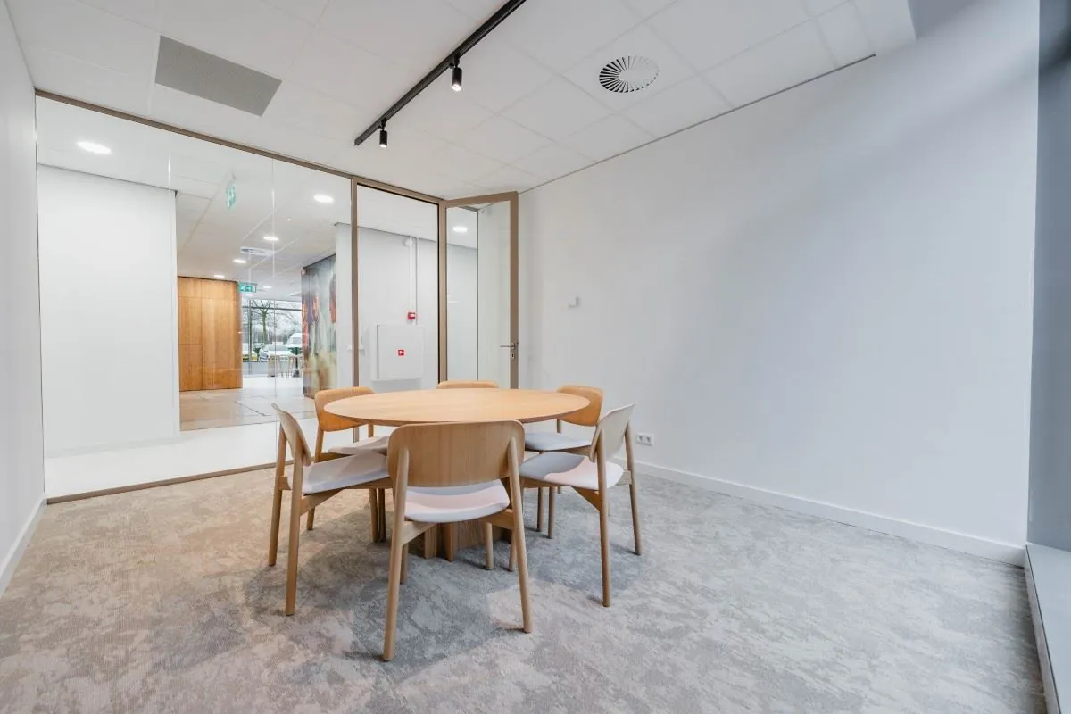 Vergaderruimte met ronde houten tafel en zes stoelen in een modern kantoorpand aan de Laarderhoogtweg 7.