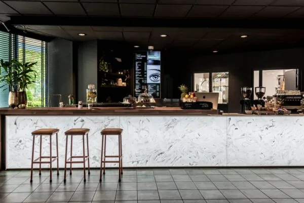 Moderne koffie- en lunchbar met marmeren toonbank, drie barkrukken en een digitaal menu aan de muur bij Lange Amerikaweg 61.