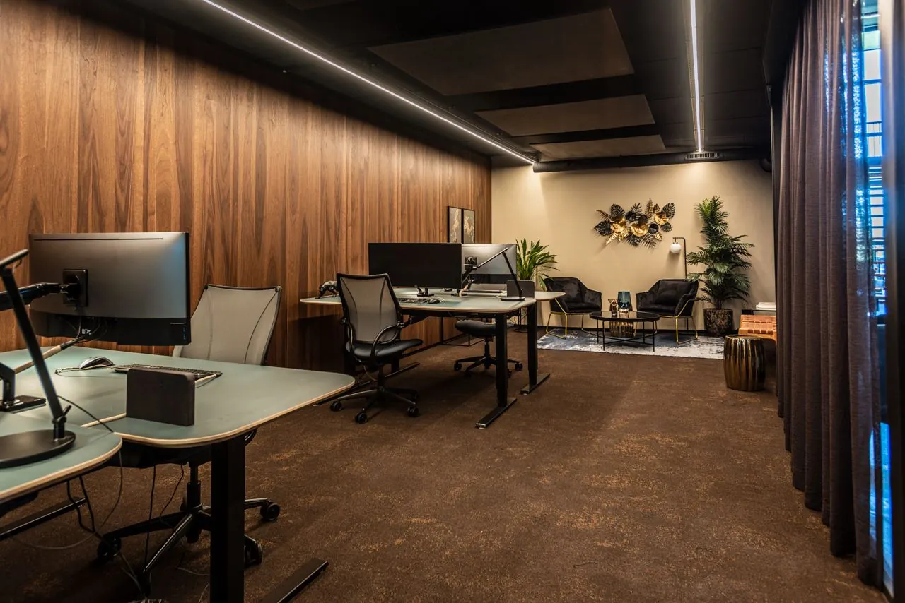 Moderne kantoorruimte aan de Lange Amerikaweg 61 met bureaus, ergonomische stoelen, en een sfeervolle zithoek met wanddecoratie en planten.