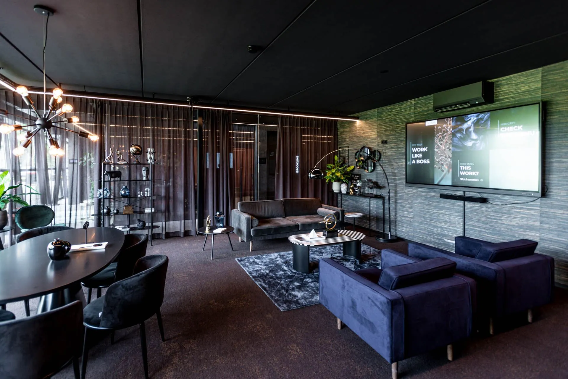 Stijlvol ingericht kantoor aan de Lange Amerikaweg 61 met moderne meubels, een grote presentatiescherm en sfeervolle verlichting.