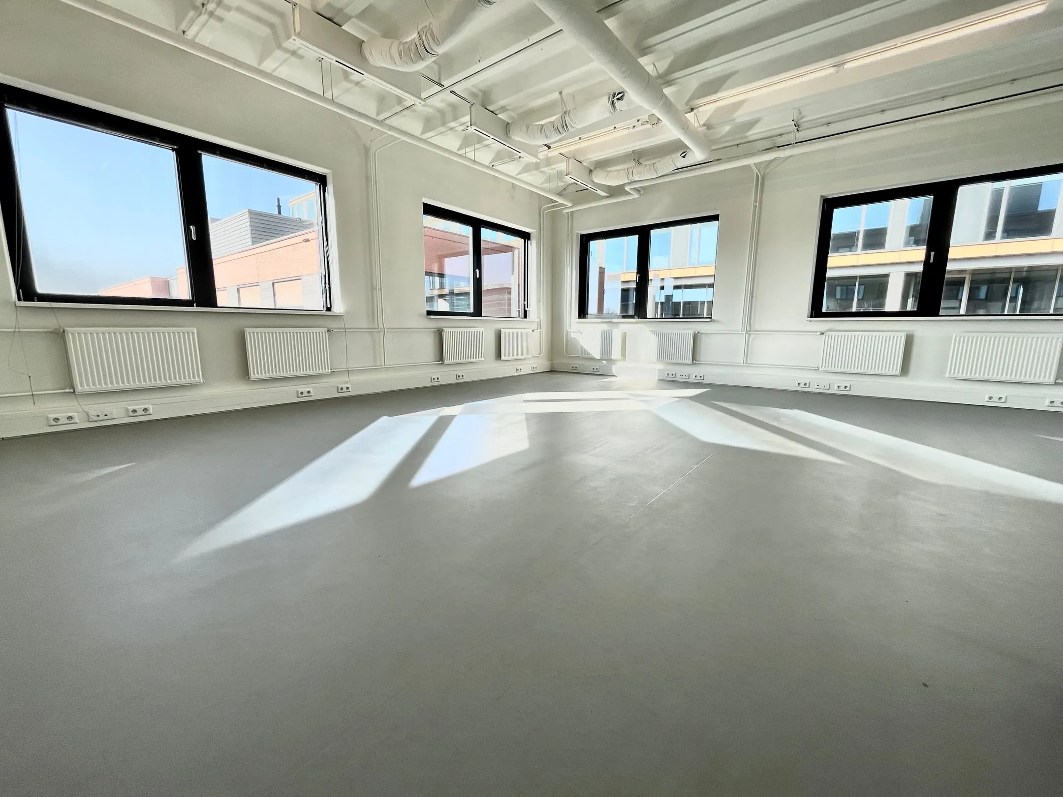 Lichte, lege kantoorruimte aan de Langekleiweg 4 met grote ramen en zicht op omliggende gebouwen.