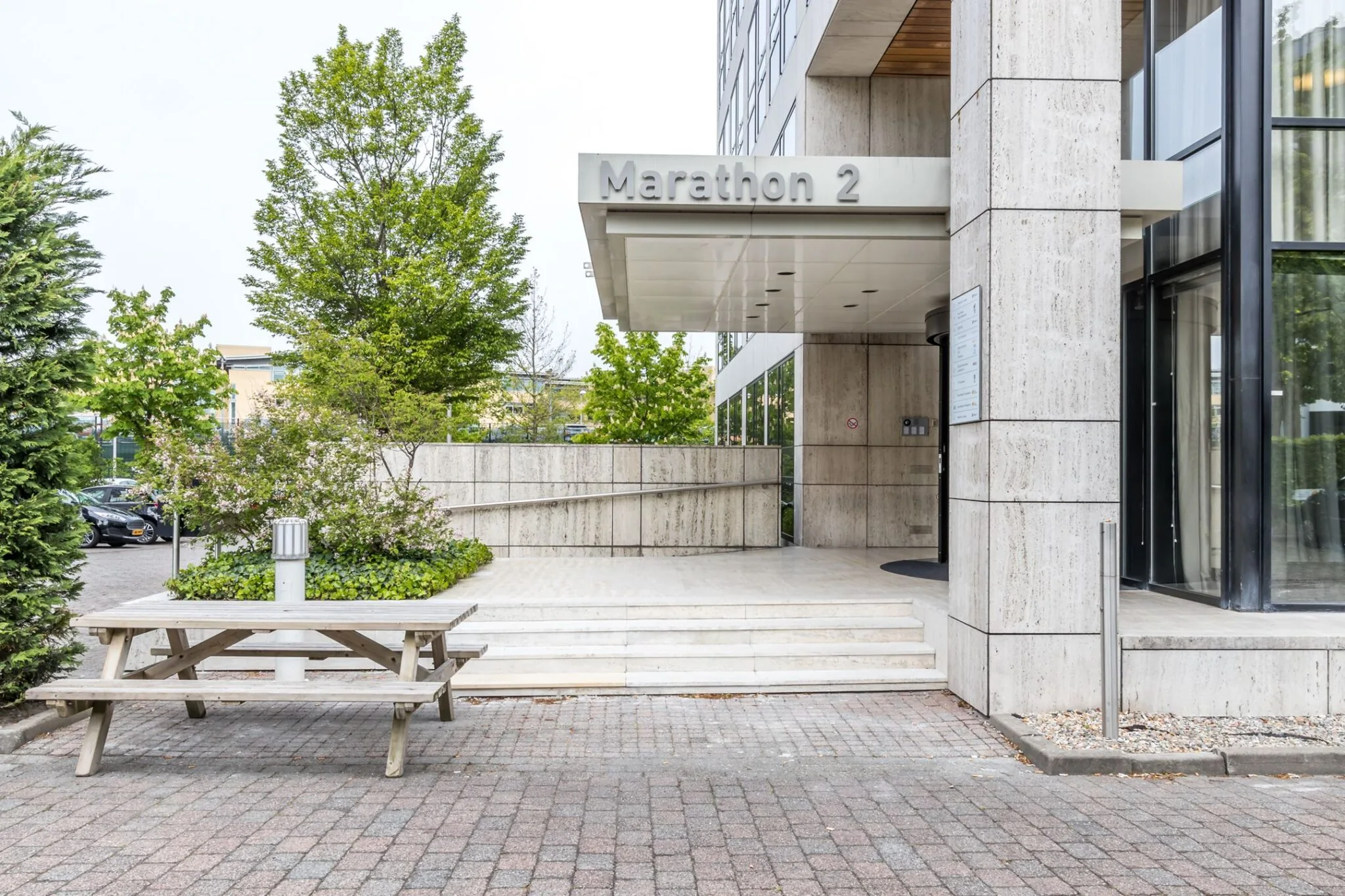 Ingang van kantoorgebouw Marathon 2 met trap, overkapping en een buitentafel op de voorgrond.