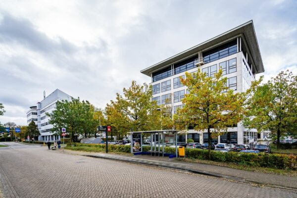 Bushalte voor het kantoorgebouw Marathon 2 met herfstkleurige bomen en geparkeerde auto's op de achtergrond.