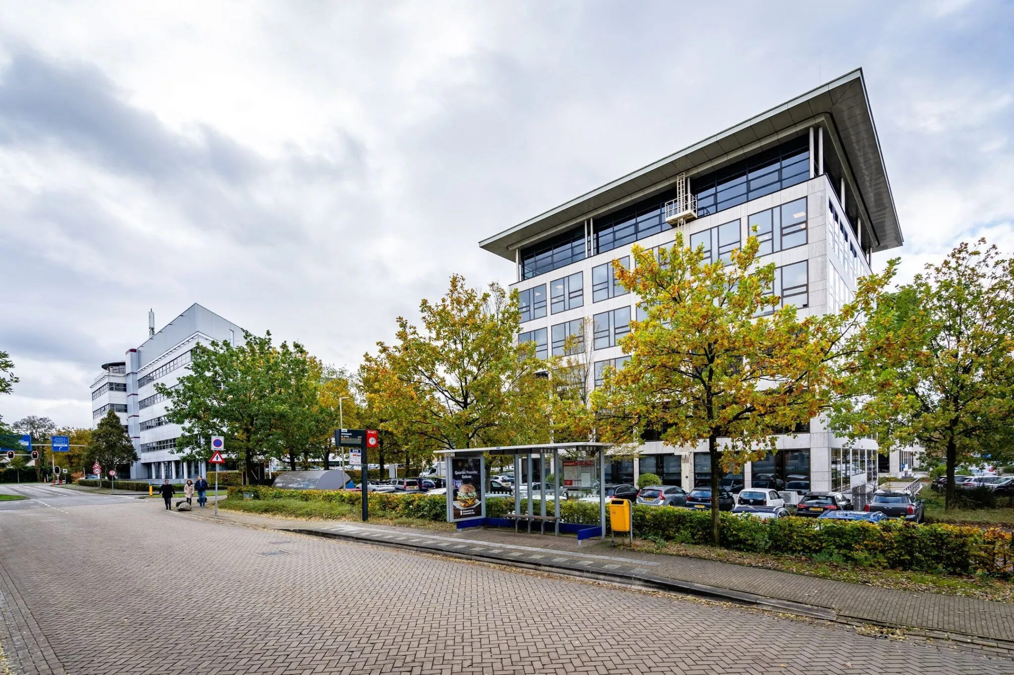 Bushalte voor het kantoorgebouw Marathon 2 met herfstkleurige bomen en geparkeerde auto's op de achtergrond.