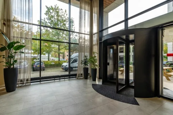 Entreehal van kantoorpand Marathon 2 met grote raampartijen, draaideur en zicht op geparkeerde auto's buiten.