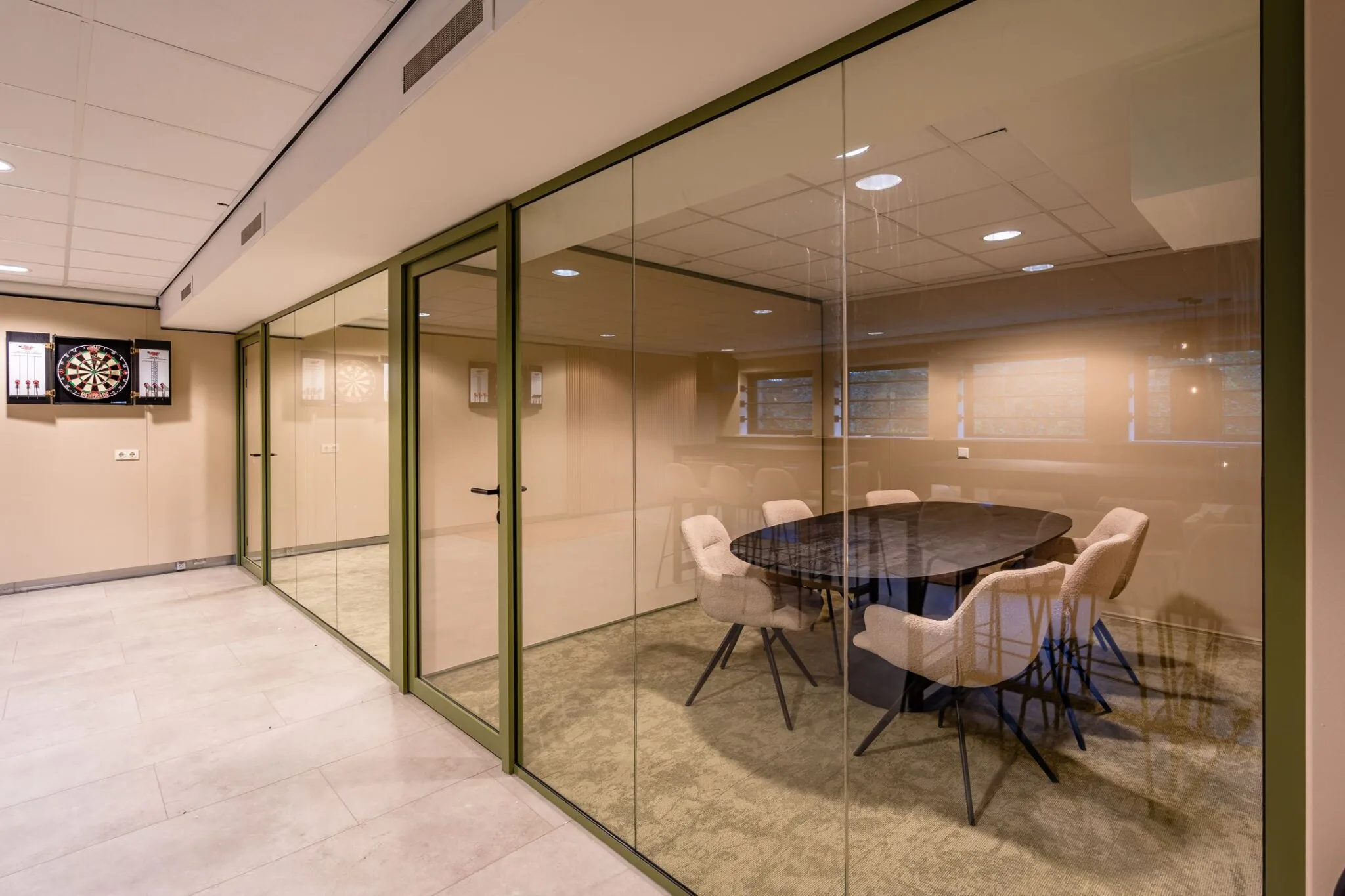 Vergaderruimte met glazen wanden, een ovale tafel met stoelen en dartborden aan de muur.