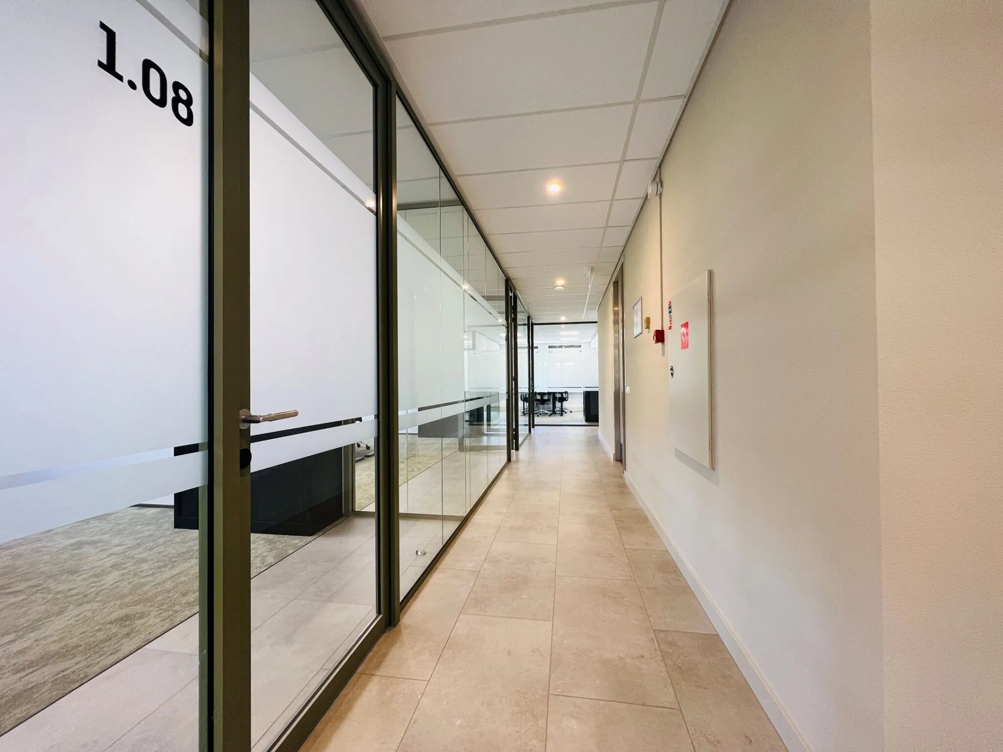 Lichte, moderne kantoor gang met glazen kantoordeuren, waaronder deur 1.08, en uitzicht op een vergaderruimte aan het einde van de gang.