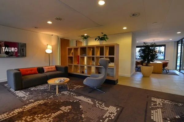 Moderne wachtruimte in kantoor aan de Marshalllaan 2 met loungezitjes, designstoel, open wandkast en kunstzinnig vloerkleed.