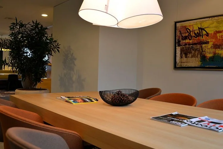 Vergaderruimte aan de Marshalllaan met houten tafel, moderne stoelen, tijdschriften en een kunstwerk aan de muur.