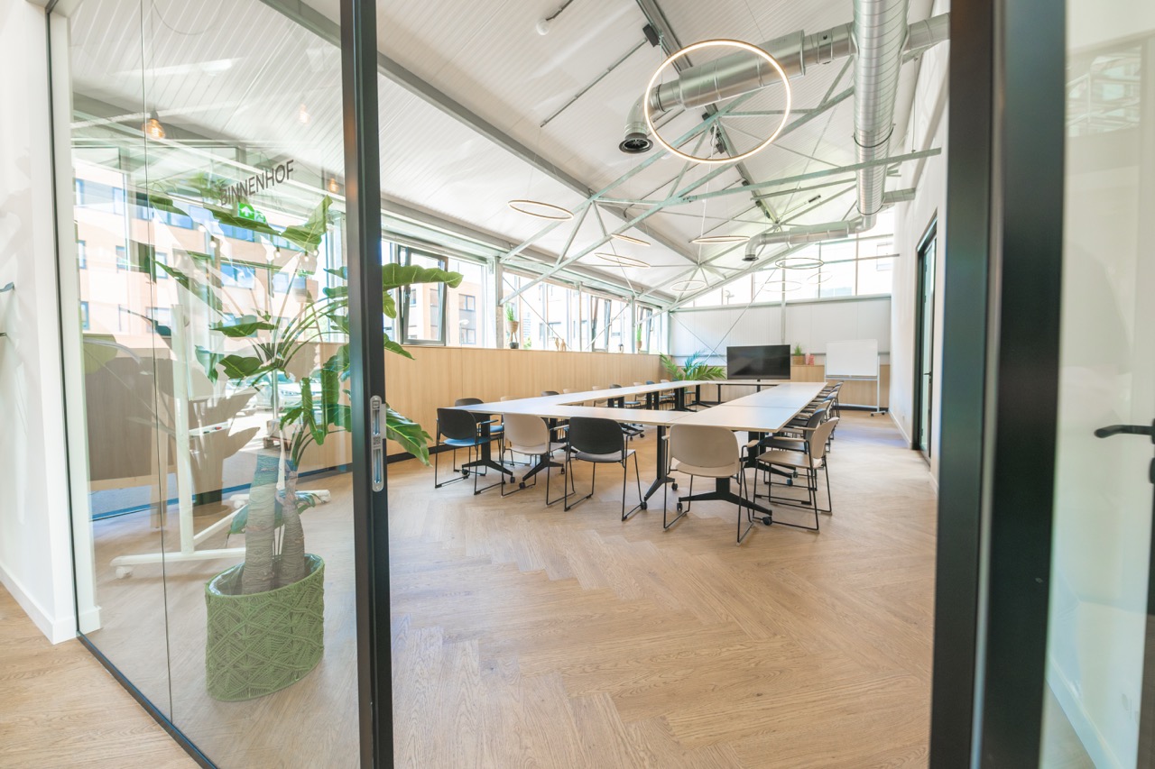 Moderne vergaderruimte Binnenhof 9 met grote tafel, diverse stoelen en veel natuurlijk licht.