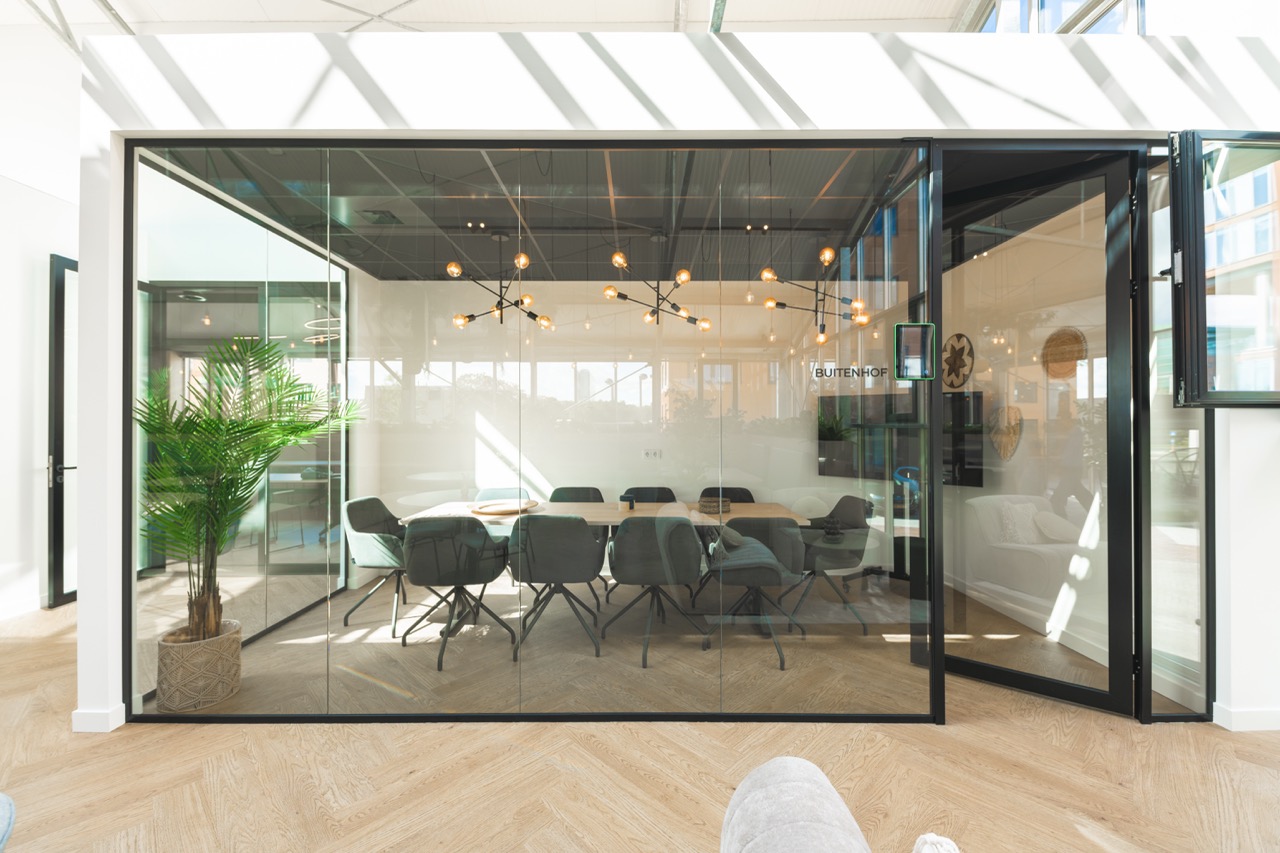 Vergaderruimte Buitenhof gezien van buitenaf met glazen wanden, moderne inrichting en een lange tafel omringd door stoelen.