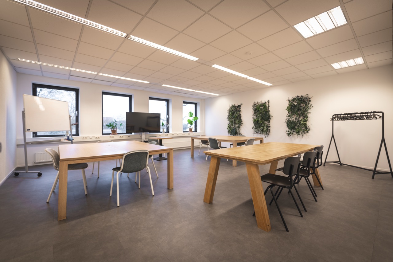 Vergaderruimte Class 3 groot met houten tafels, diverse stoelen, een whiteboard, flatscreen en groene wanddecoratie.