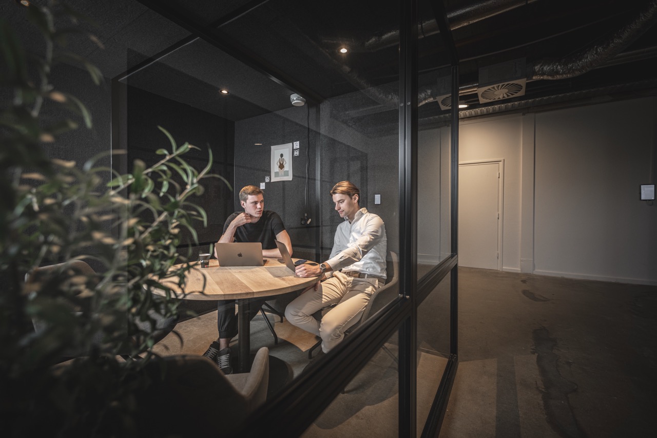 Twee mannen zitten in vergaderruimte Klok aan een ronde tafel te werken met laptops.