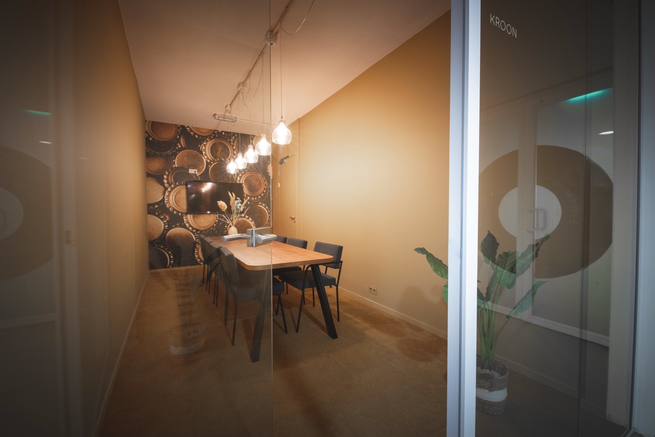 Vergaderruimte Kroon met glazen wanden, een houten tafel, zes stoelen en decoratieve kurken op de achterwand.
