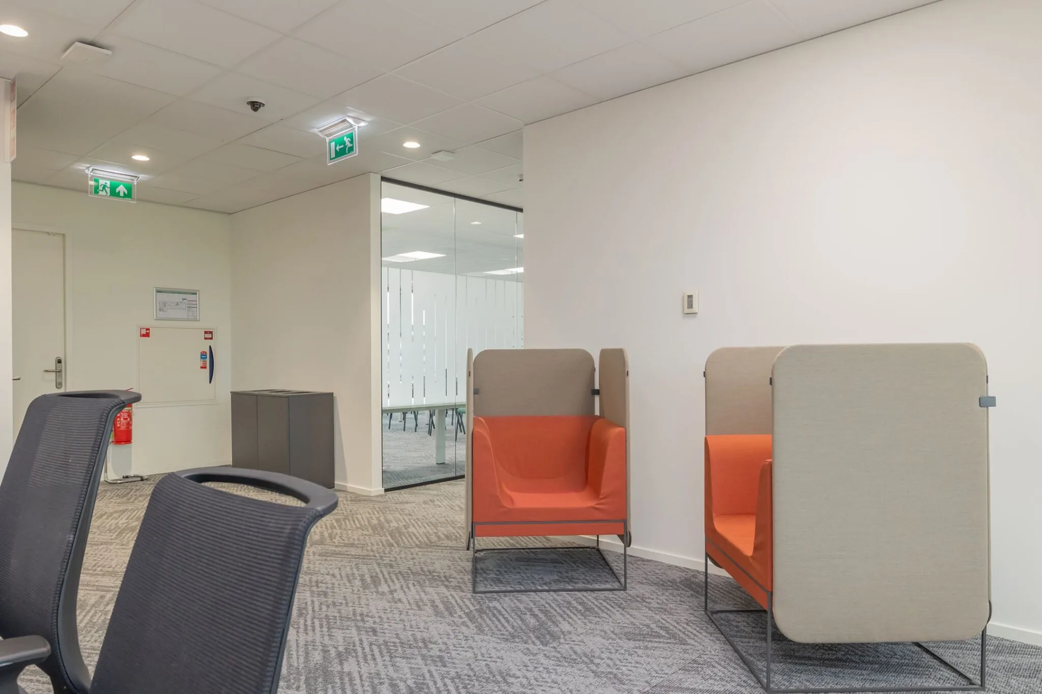 Moderne wachtruimte met twee oranje akoestische stoelen en zicht op een glazen vergaderruimte bij Mendelweg 32.