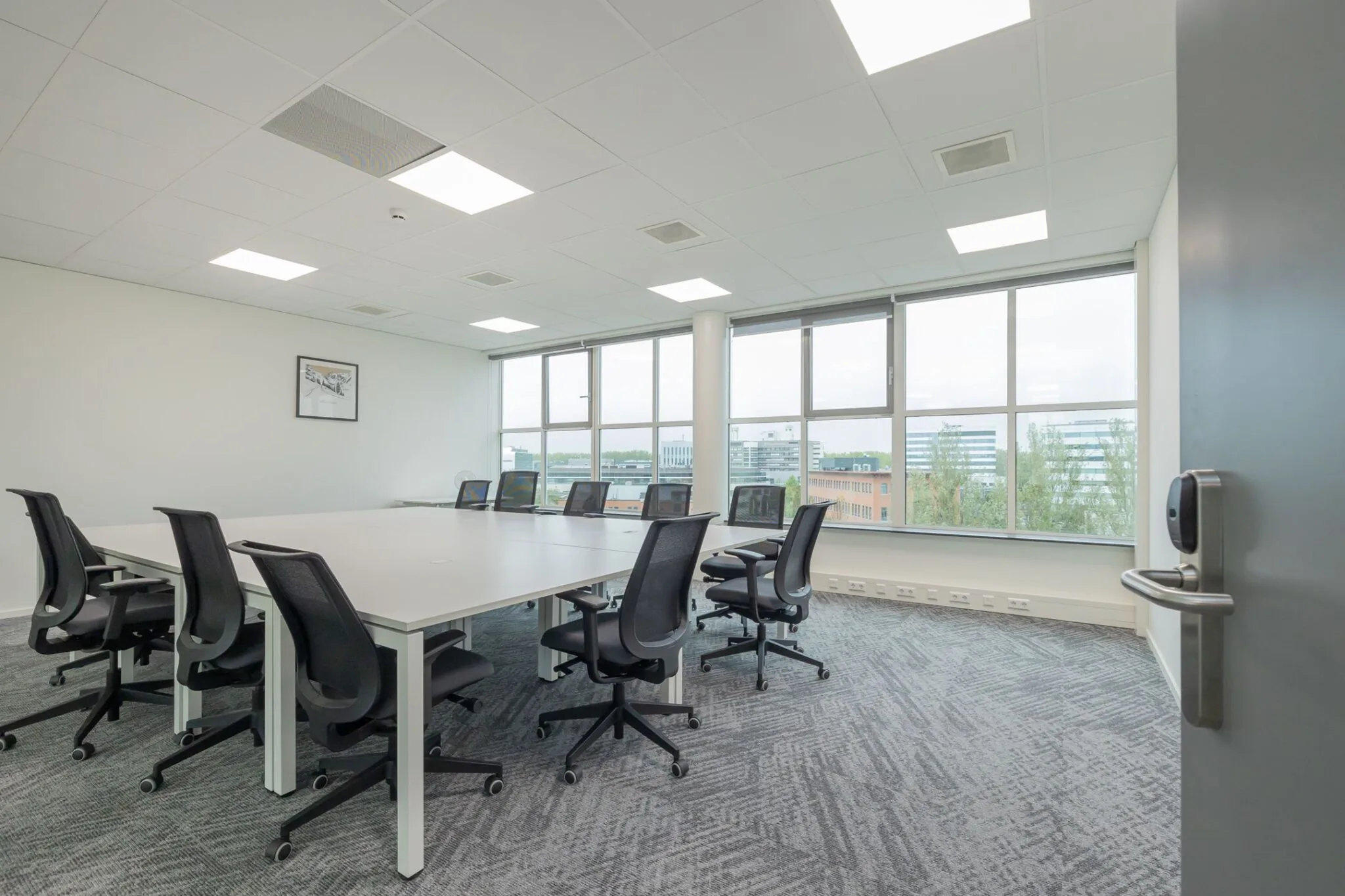 Vergaderruimte met grote tafel, zwarte bureaustoelen en ramen met uitzicht op kantoorgebouwen aan de Mendelweg 32.