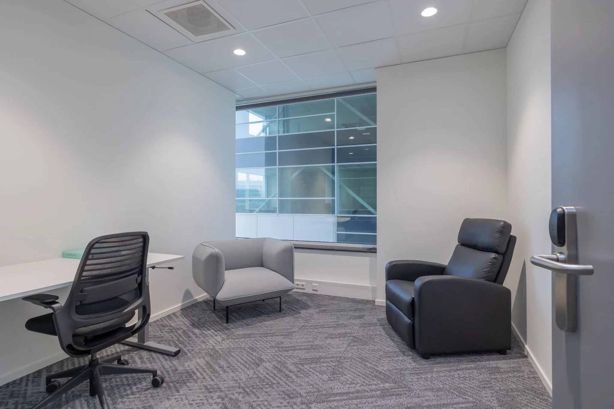 Moderne, minimalistisch ingerichte kantoorruimte op Mendelweg 32 met bureau, bureaustoel en twee comfortabele fauteuils.
