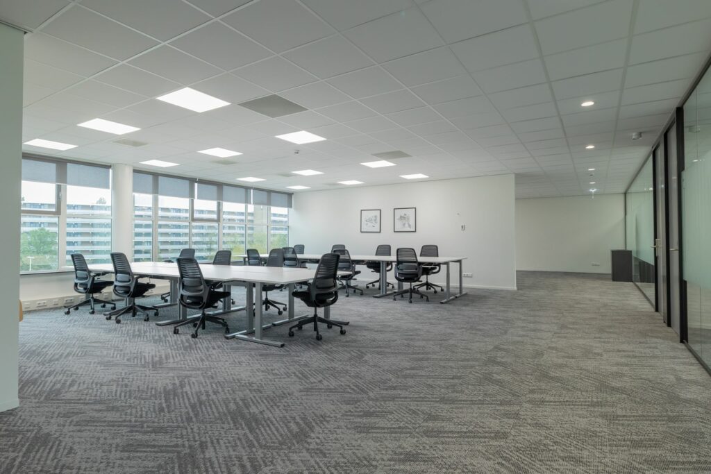 Ruime, moderne kantoorruimte aan de Mendelweg 32 met bureaus, bureaustoelen en grote ramen met uitzicht op een appartementencomplex.