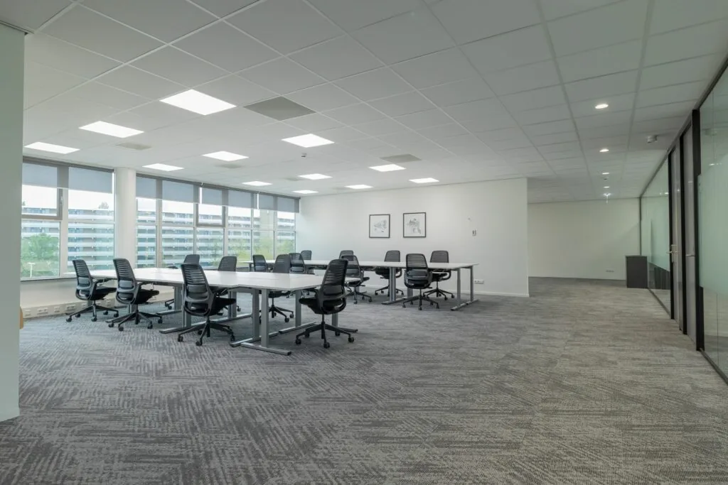 Ruime, moderne kantoorruimte aan de Mendelweg 32 met bureaus, bureaustoelen en grote ramen met uitzicht op een appartementencomplex.