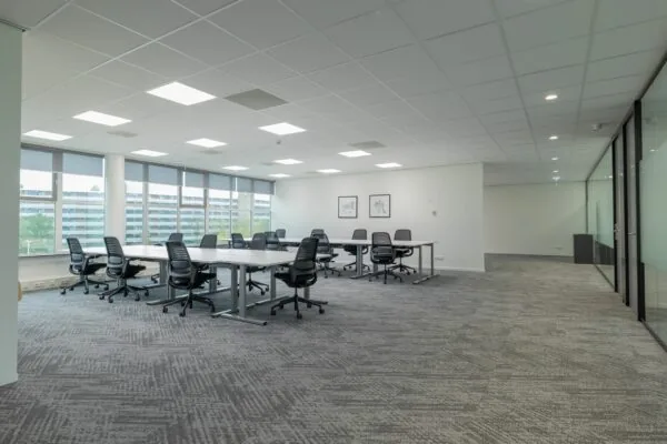 Ruime, moderne kantoorruimte aan de Mendelweg 32 met bureaus, bureaustoelen en grote ramen met uitzicht op een appartementencomplex.