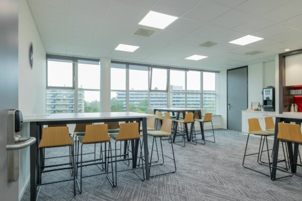 Moderne kantoorkantine met hoge tafels, houten barkrukken en een koffiecorner bij Mendelweg 32.