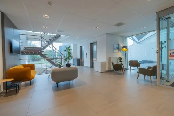 Moderne wachtruimte in een kantoorgebouw aan de Mendelweg 32 met zitgelegenheid, liftdeuren en een open trap.