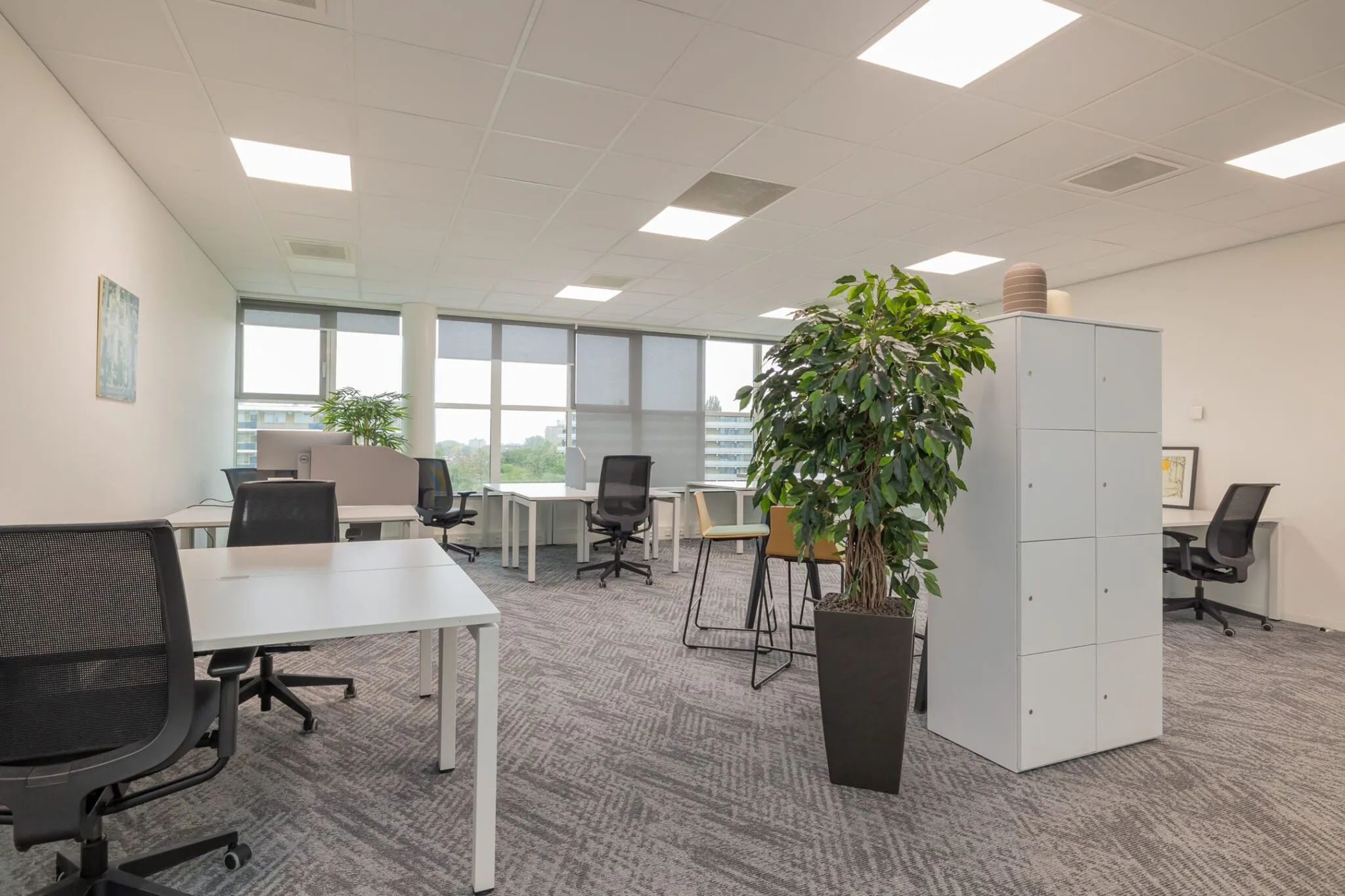 Moderne, lichte kantoorruimte aan de Mendelweg 32 met bureaus, bureaustoelen, een plantenbak en lockerkast.