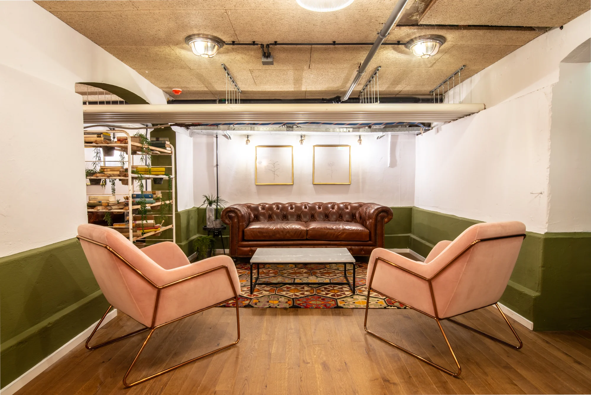 Stijlvolle loungehoek bij Mindspace Utrecht met een bruine leren bank, roze stoelen en kleurrijk vloerkleed.