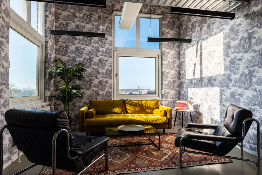 Zonnige loungehoek in Mindspace Utrecht met een gele bank, zwarte fauteuils en vintage behang.