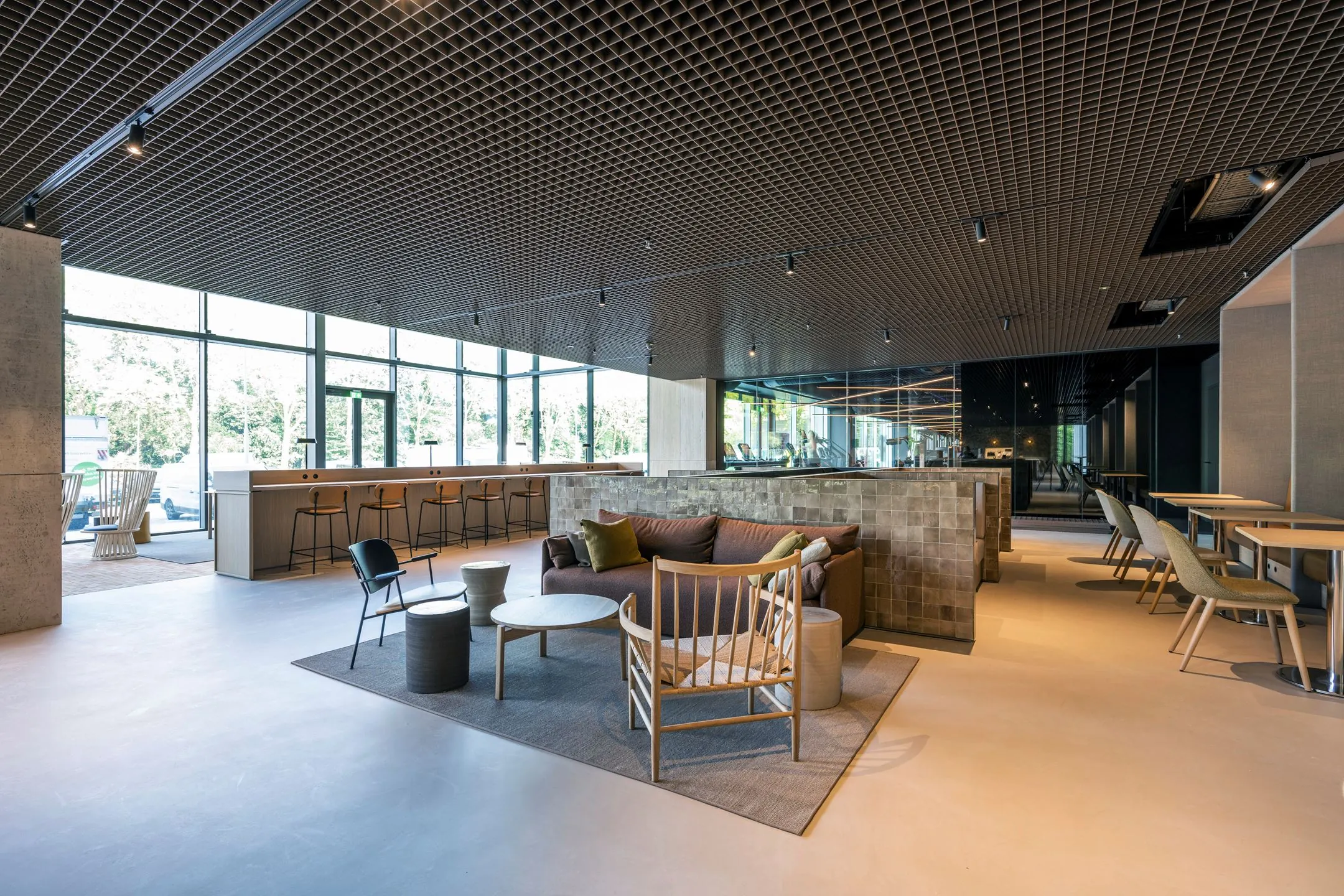 Moderne en ruimtelijke lounge- en werkruimte met zitplaatsen, hoge ramen en een industriële plafondafwerking in Nachtwachtlaan 20.