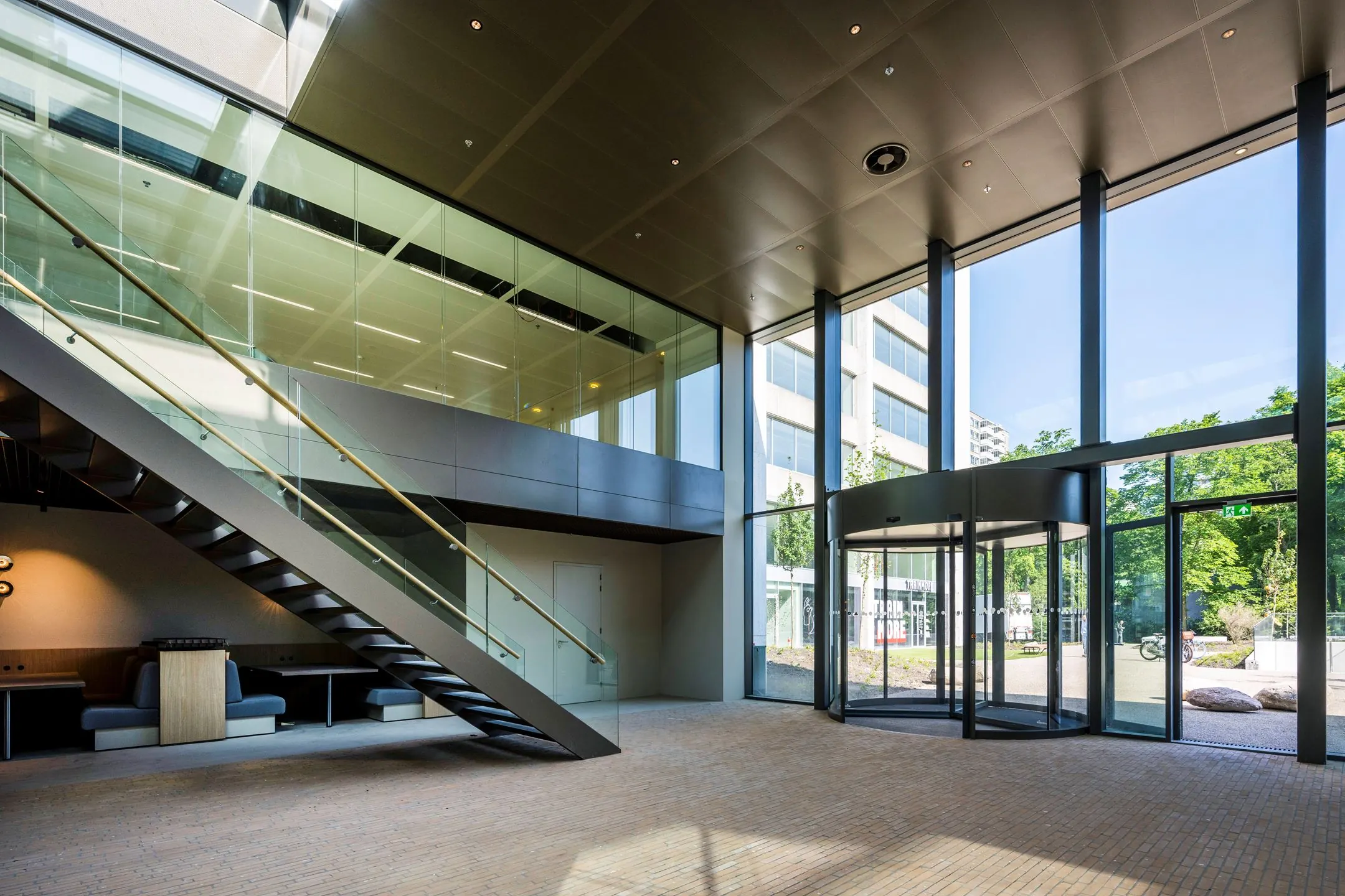 Moderne entreehal van kantoorgebouw aan de Nachtwachtlaan 20 met glazen gevel, trap en draaideur.