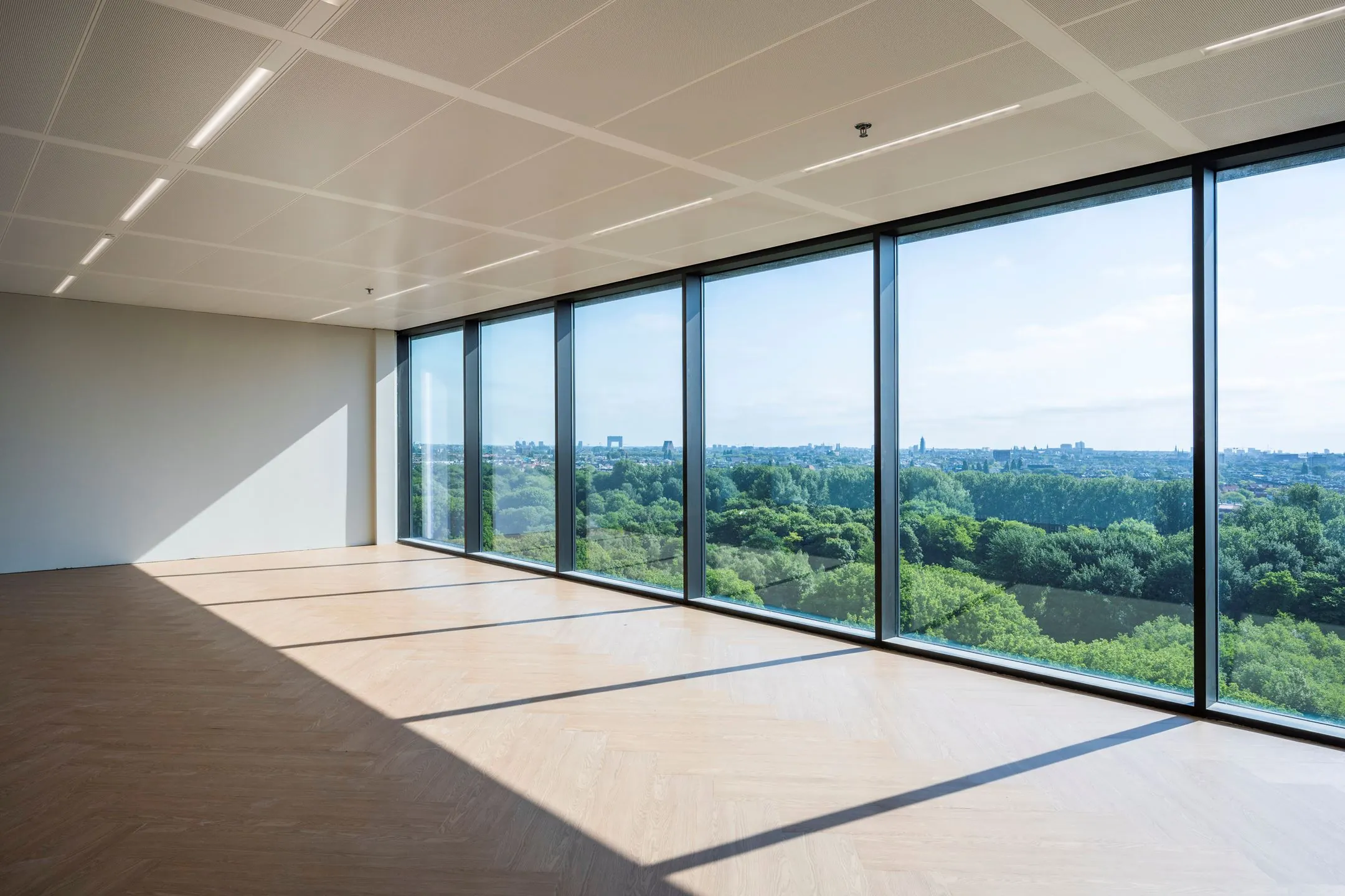 Lichte, lege kantoorruimte aan de Nachtwachtlaan met groot raam en uitzicht op groen en skyline.