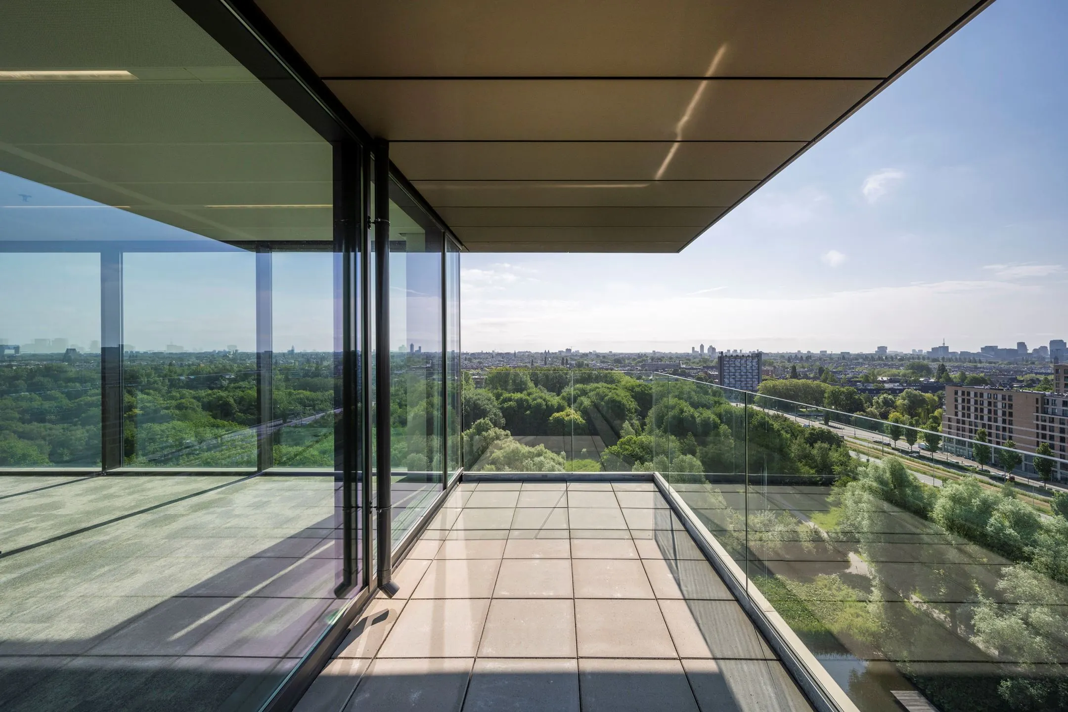 Uitstekend uitzicht vanaf een modern balkon met glazen balustrade aan de Nachtwachtlaan 20, met zicht op groen en stad.