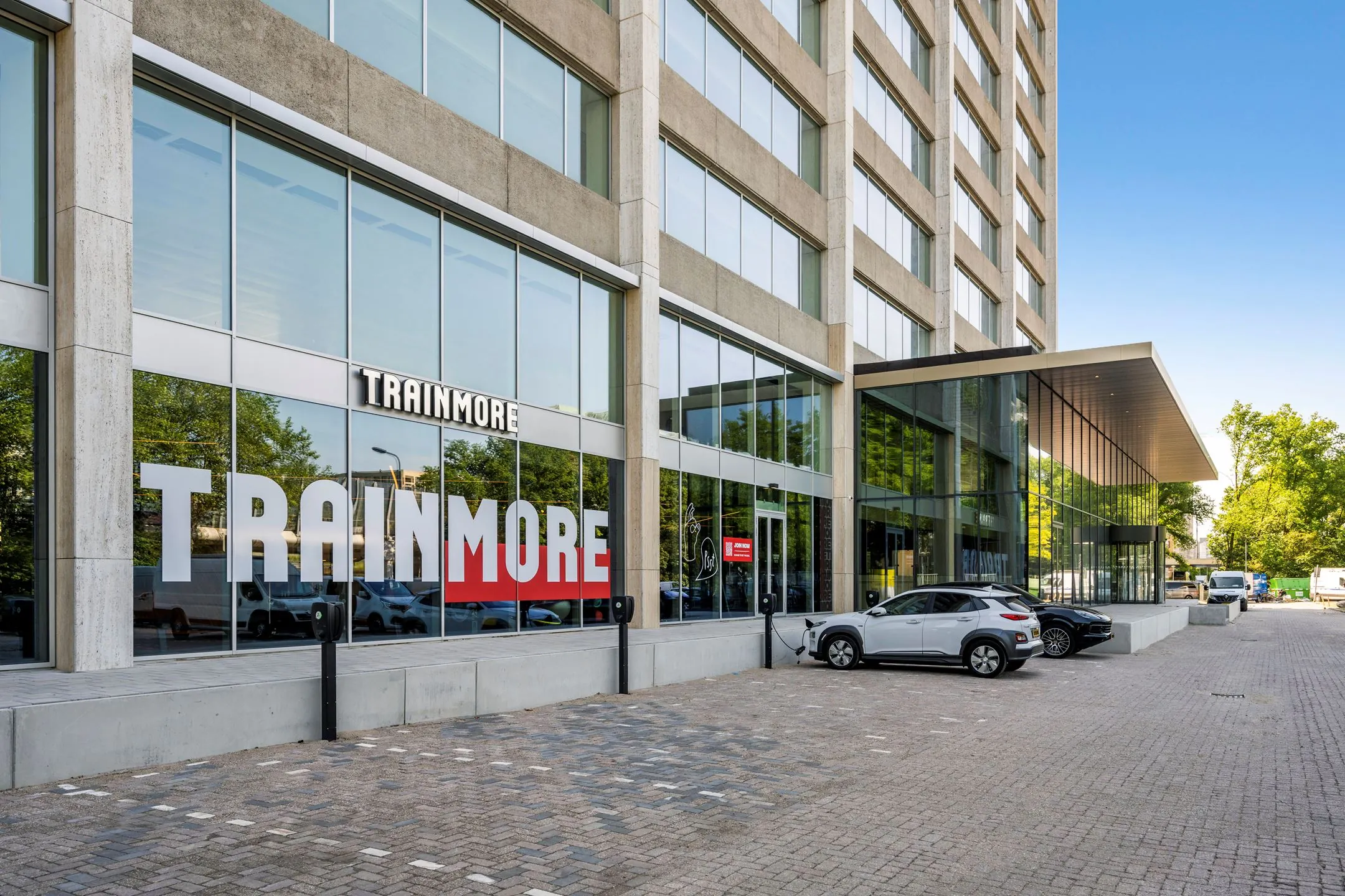 Vooraanzicht van het gebouw aan de Nachtwachtlaan 20 met de ingang van sportschool TrainMore en geparkeerde auto’s op de oprit.