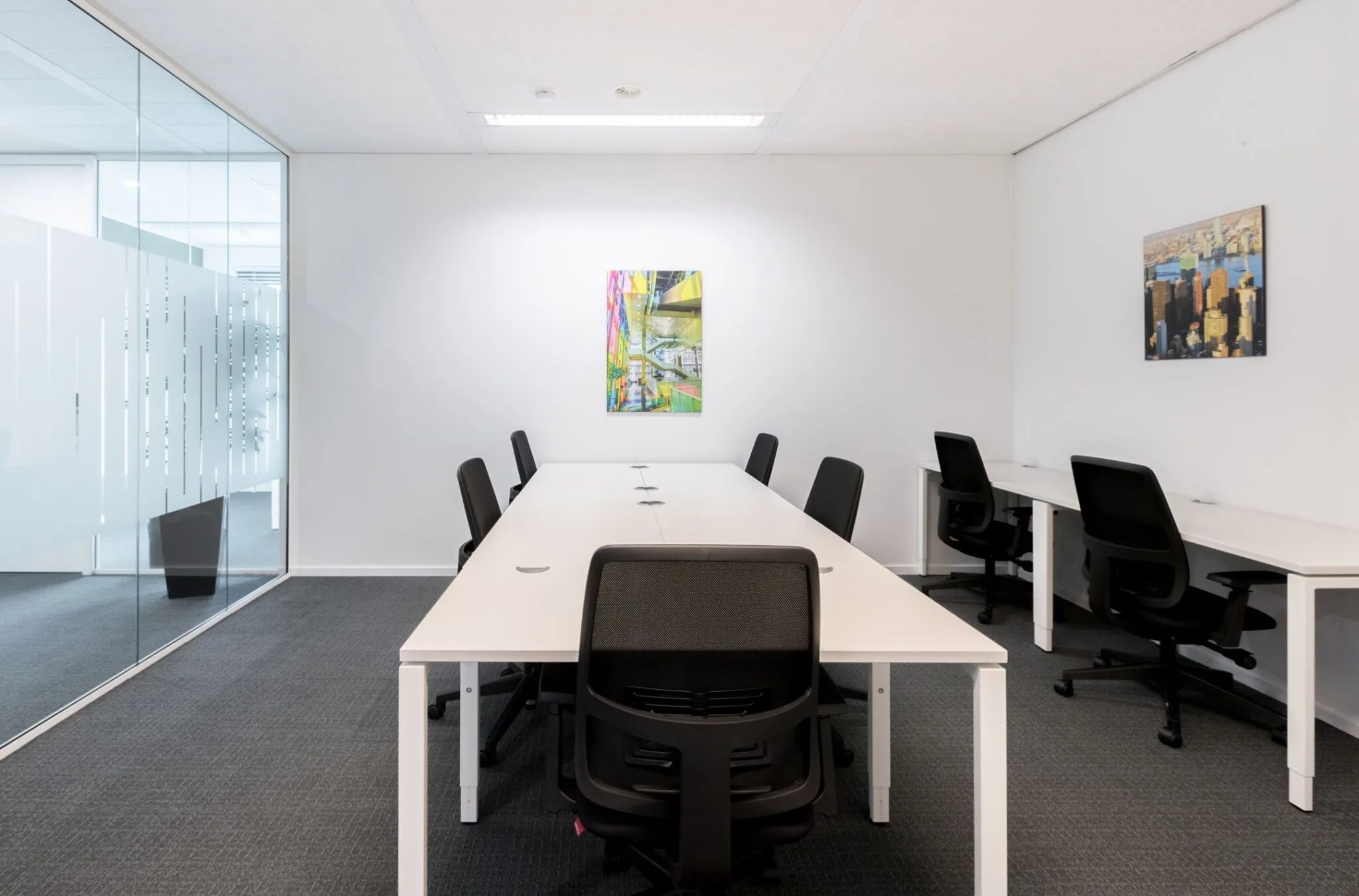 Moderne kantoorruimte met witte bureaus, zwarte bureaustoelen en kleurrijke kunst aan de muur bij Nevelgaarde 8.