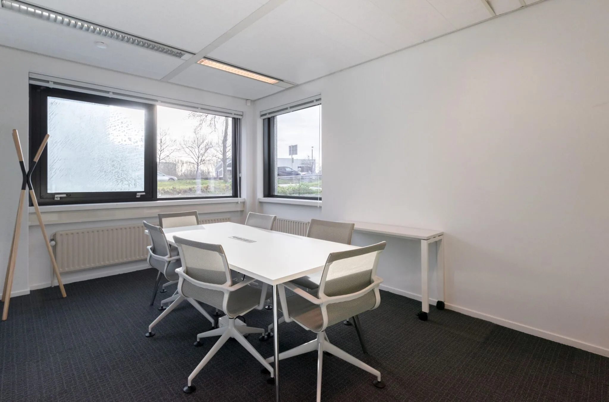 Vergaderruimte met een witte tafel, zes bureaustoelen en grote ramen in het kantoor aan Nevelgaarde 8.