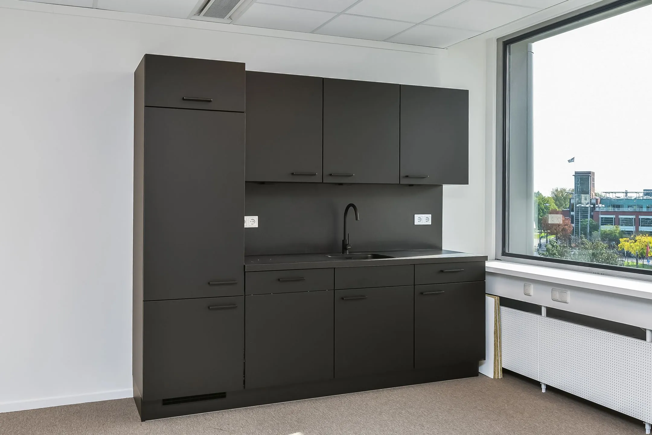 Zwarte keukenblok met spoelbak in een modern kantoor bij Newday Arnhem, naast een groot raam met uitzicht.