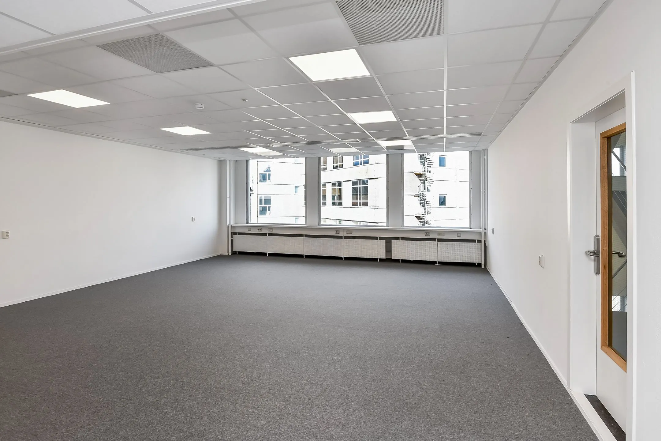 Lichte, lege kantoorruimte in Newday Arnhem met grijze vloerbedekking en grote ramen.