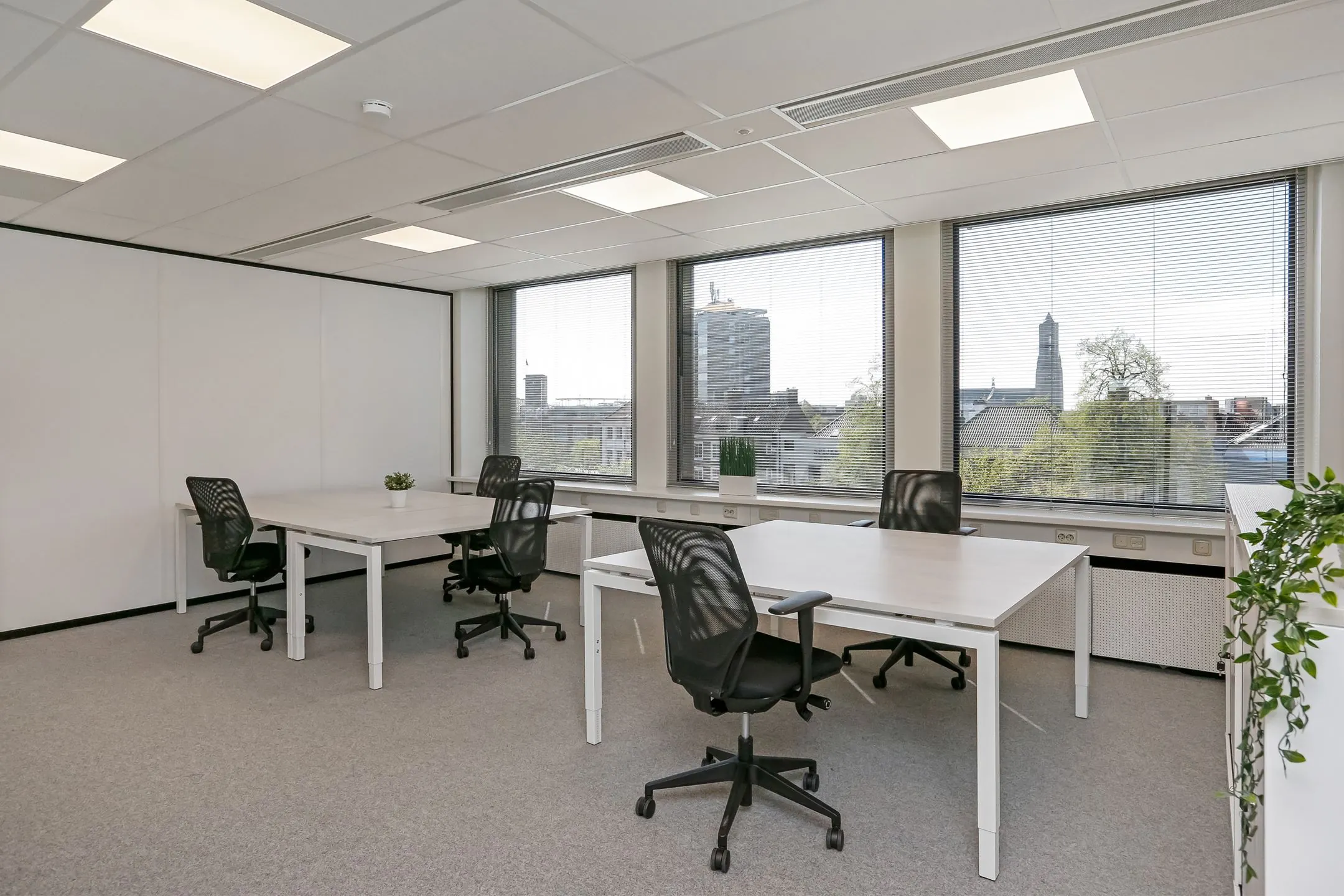 Modern kantoorruimte bij Newday Arnhem met vier bureaus, ergonomische stoelen en uitzicht op de stad.