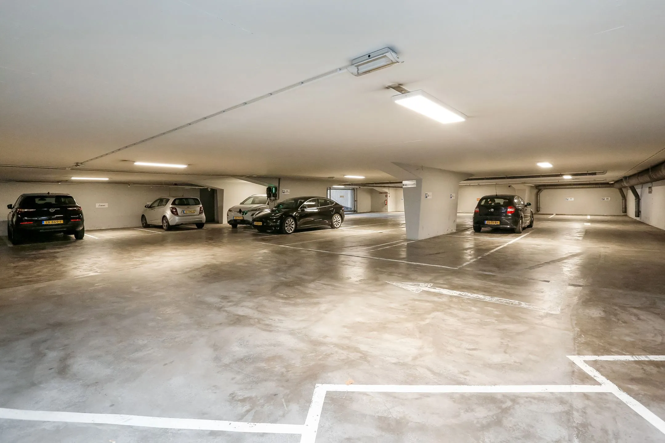 Ondergrondse parkeergarage bij Newday Arnhem met meerdere geparkeerde auto's en oplaadpunt voor elektrische voertuigen.