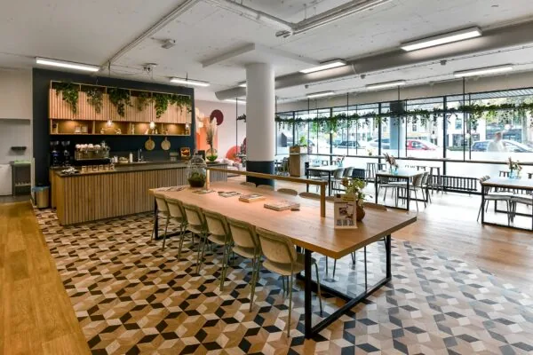 Moderne en sfeervolle ontmoetingsruimte van Newday Arnhem met een koffiebalie, lange houten tafel en grote ramen met uitzicht op de straat.